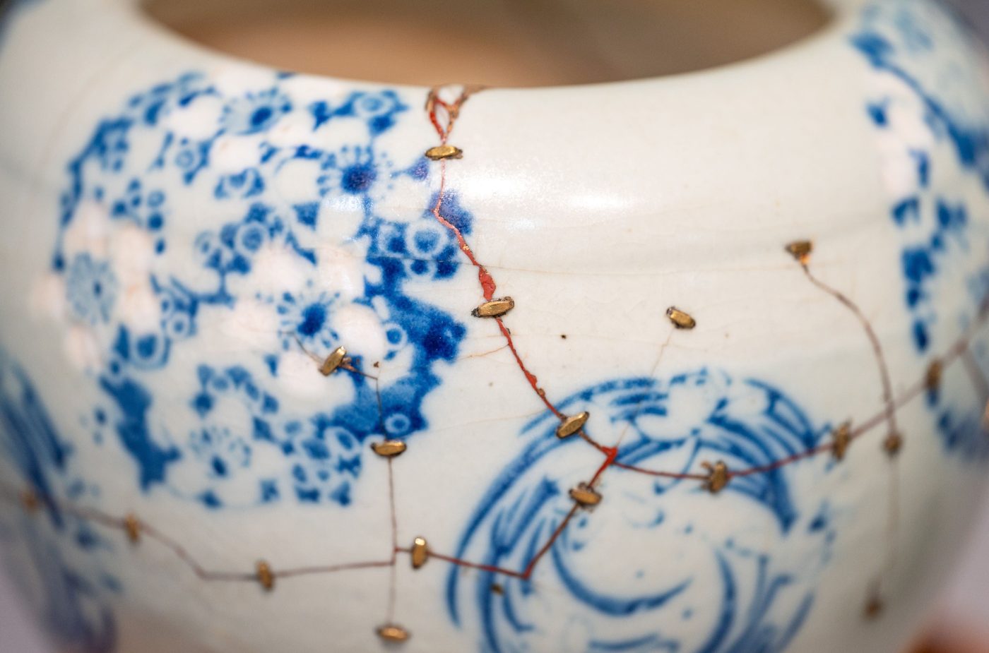 A blue-and-white porcelain jar, its cracks drawn together by rows of small metal staples.