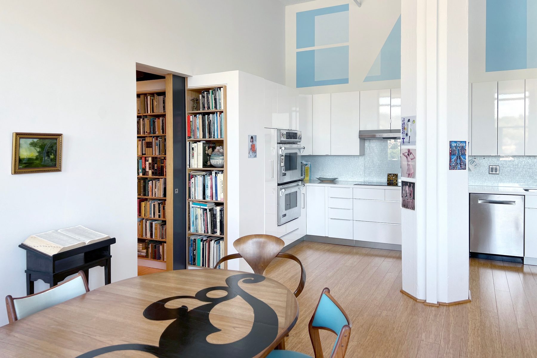 An apartment interior with bookshelves flanking a doorway and a white kitchen beyond