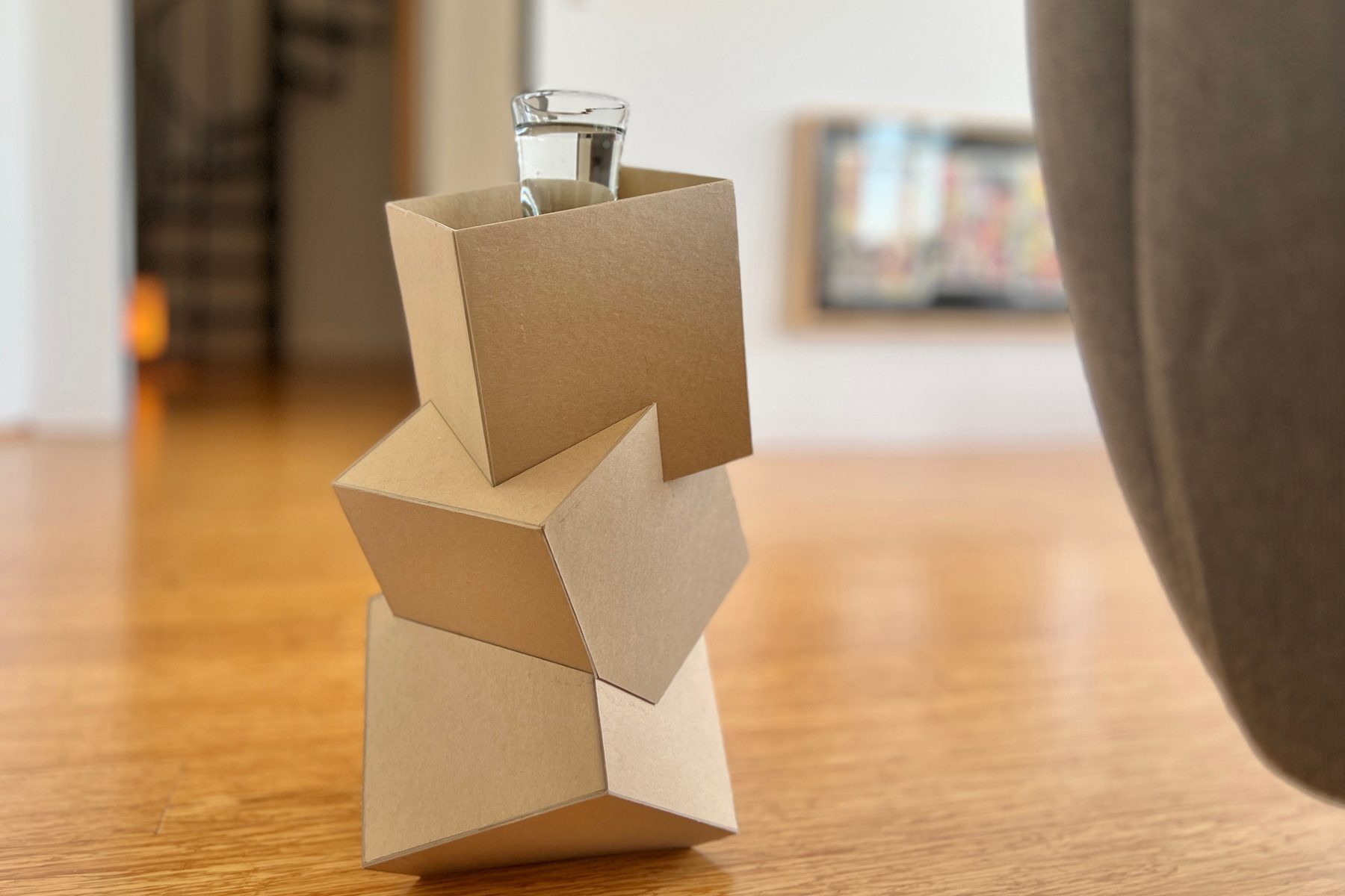 A faceted cardboard massing model standing on a wood floor